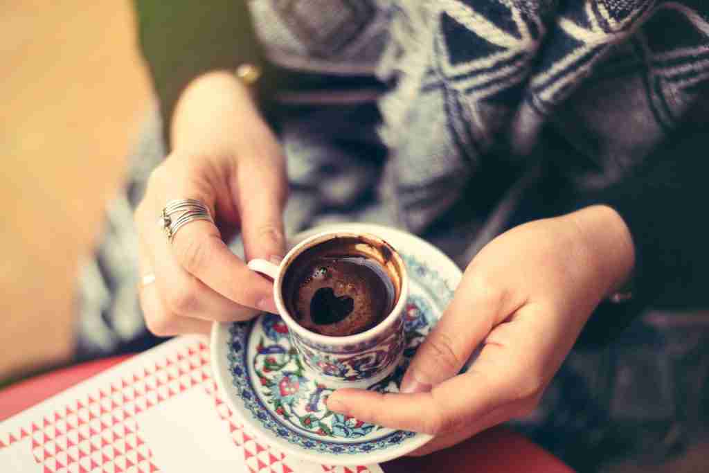 Hands holding a cup of Turkish coffee with a heart shape in the foam
